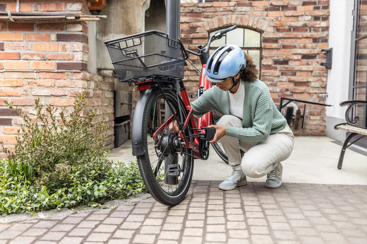 Una donna blocca la sua bicicletta a una colonna con un BORDO One 6000 e indossa un casco da bici HUD-Y in blu ghiaccio © ABUS