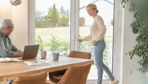 Eine Frau öffnet eine Terrassentür, die mit dem Stangenschloss FOS650 und der Scharnierseitensicherung FAS101 gesichert ist © ABUS
